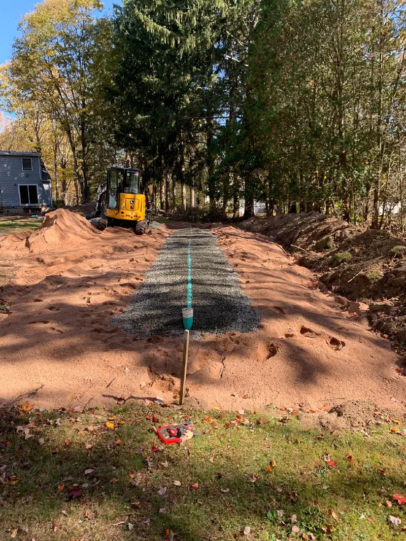 New leaching field with a gravel bed and inspection port, a mini excavator behind it