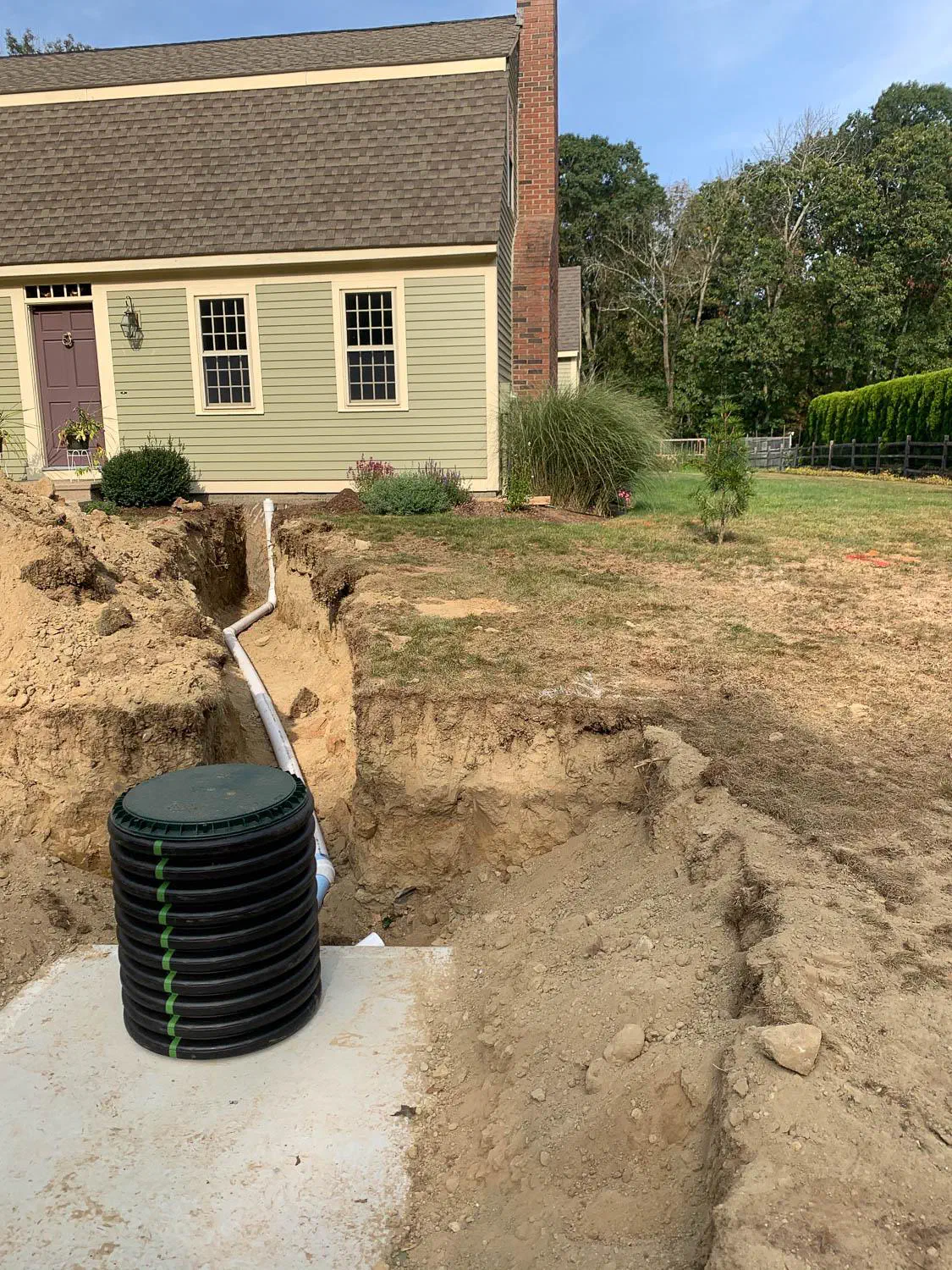 New tank riser and pipe trench beside a green colonial home