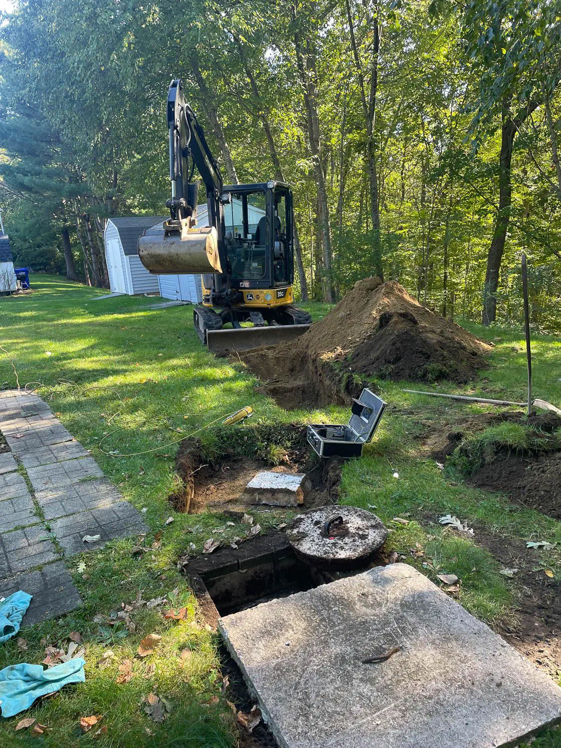 Mini excavator beside an uncovered septic tank in a back yard