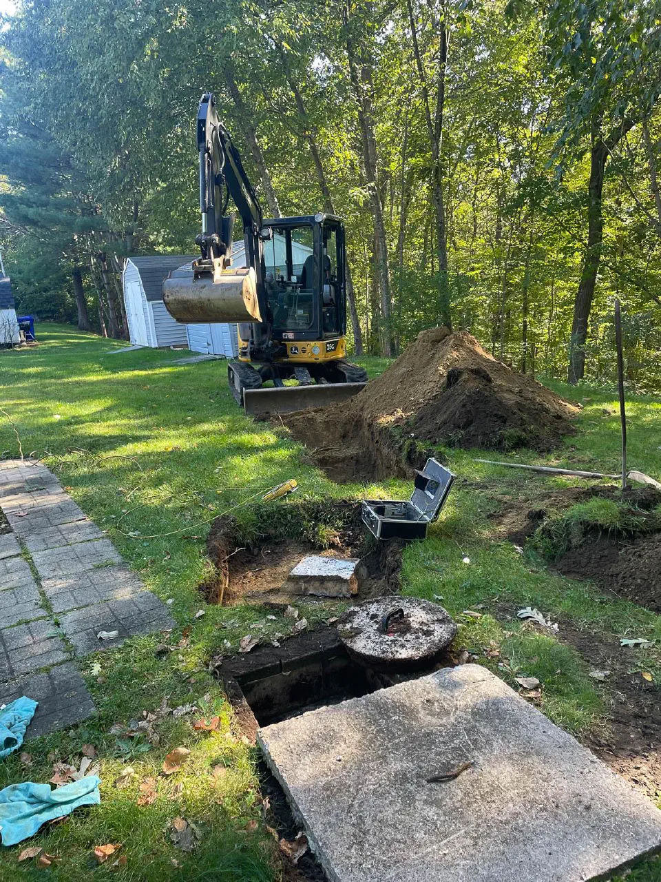 Mini excavator beside an uncovered septic tank in a back yard