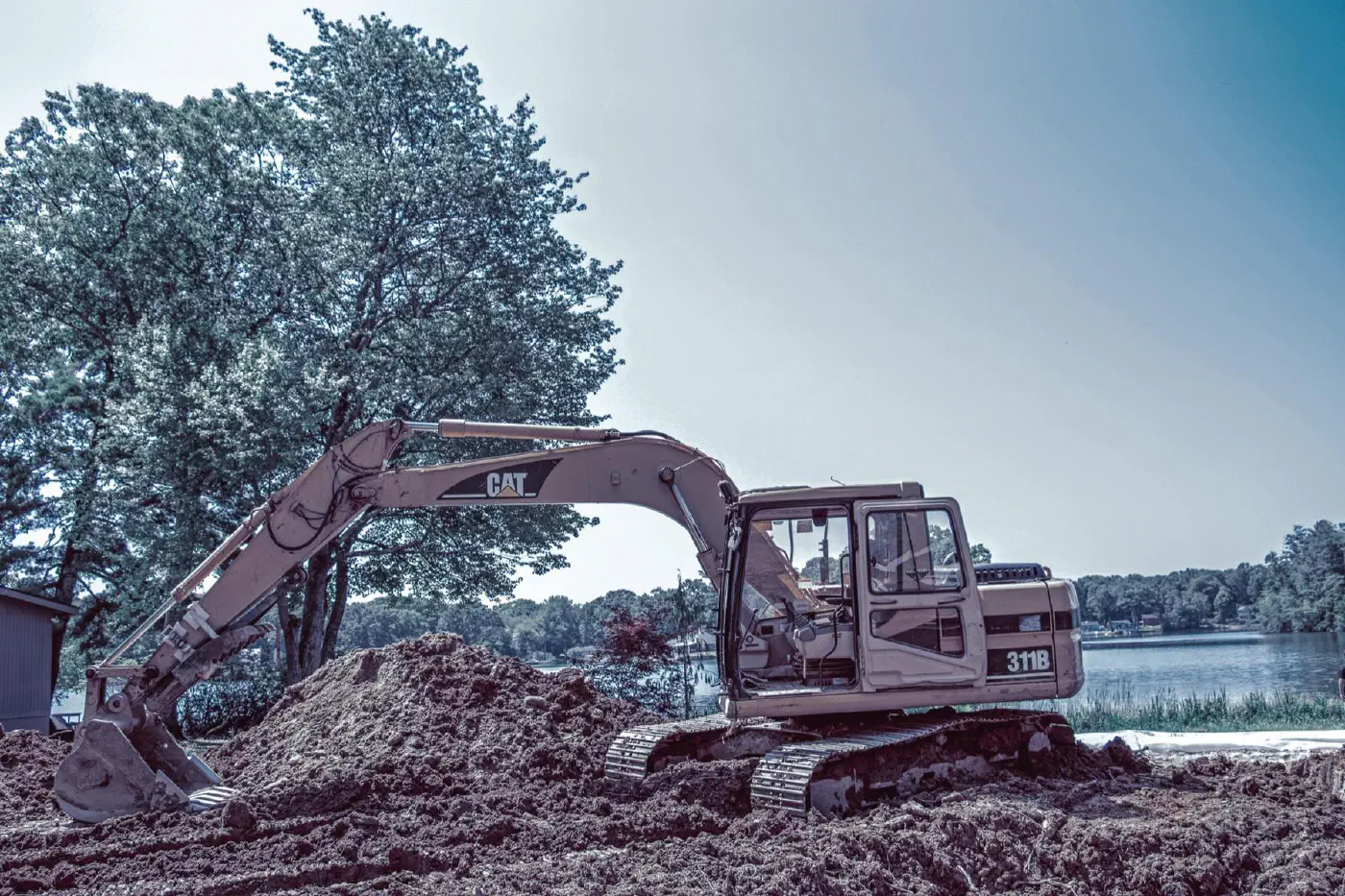 CAT excavator on a mound of excavated soil at a lakeside job site